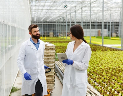 Twee wetenschappers in laboratoriumjassen die in een plantenkas lopen binnen de sector Food en Pharma